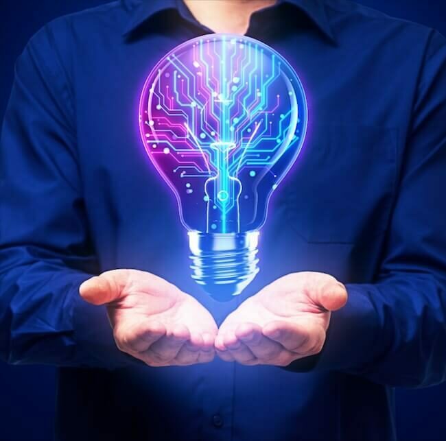 A person in a blue shirt holds their hands open, and a glowing light bulb with circuit patterns floats above them against a dark background. The bulb symbolizes innovation and technology.
