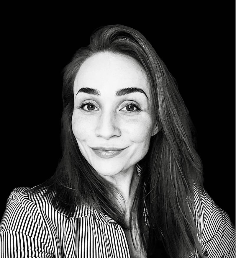 Emisa Lehtinen Black and white portrait of a woman with long hair, smiling softly. She wears a striped shirt and looks directly at the camera, against a solid black background.