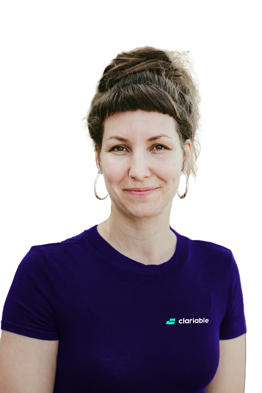 Valena A woman with brown hair in a bun, wearing hoop earrings and a purple "clarable" t-shirt, stands outdoors and smiles softly at the camera with green foliage blurred in the background.